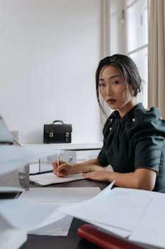 Asian woman focused on paperwork in an office setting, showcasing a modern business environment.
